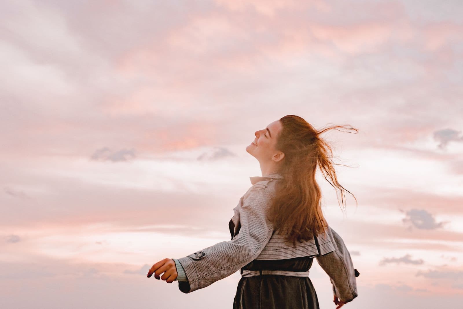 A woman outdoors at sunset, head lifted and relaxed, feeling free.